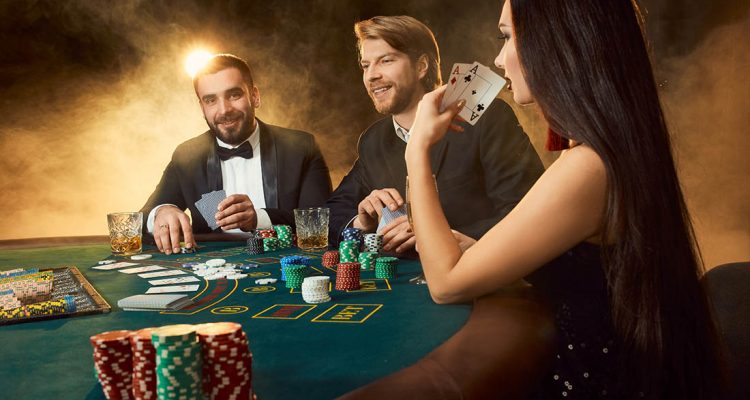 Group of young rich people is playing poker in the casino. Two men in business suits and a young woman in a black dress. Smoke. Casino. Poker